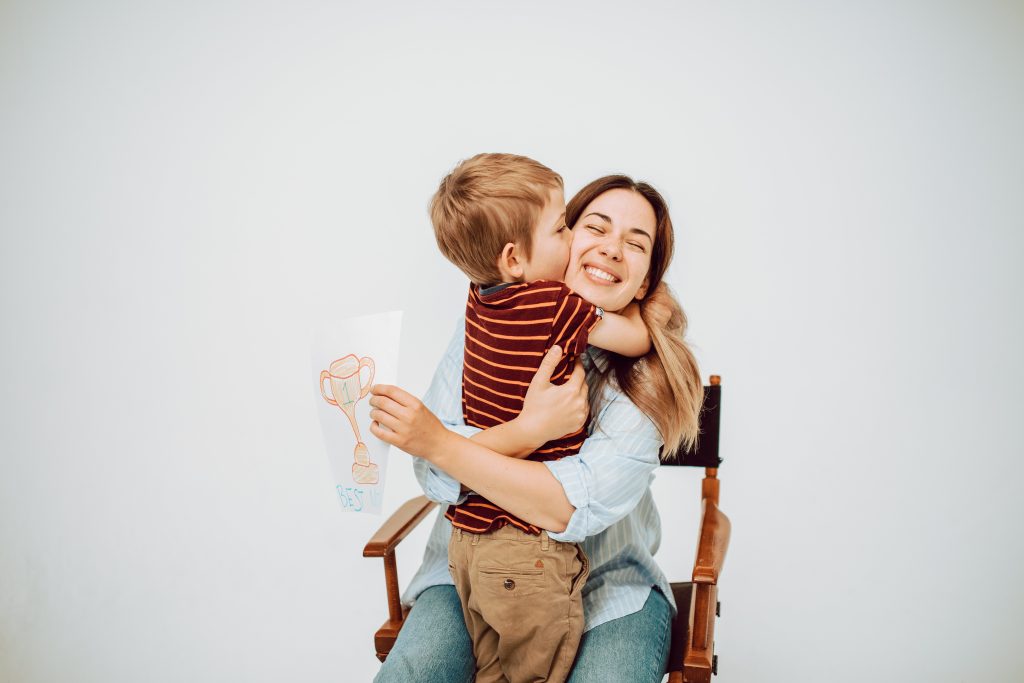 A joyful child hugging his smiling mother while holding a trophy drawing.