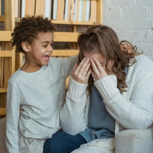 Mother and son sharing a joyful moment playing peekaboo indoors with laughter and warmth.