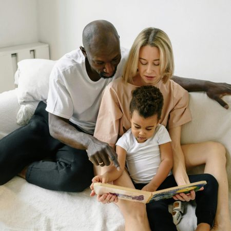 A family enjoys reading time together on a cozy white sofa indoors.