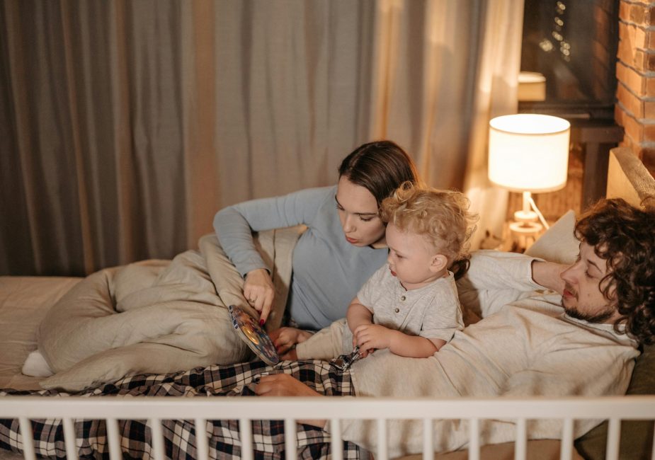 Father and mother reading to their child in bed during nighttime for a cozy bedtime story.